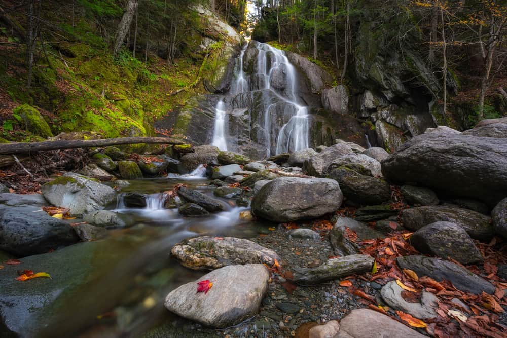 Two waterfalls going into a pond by dark trees.