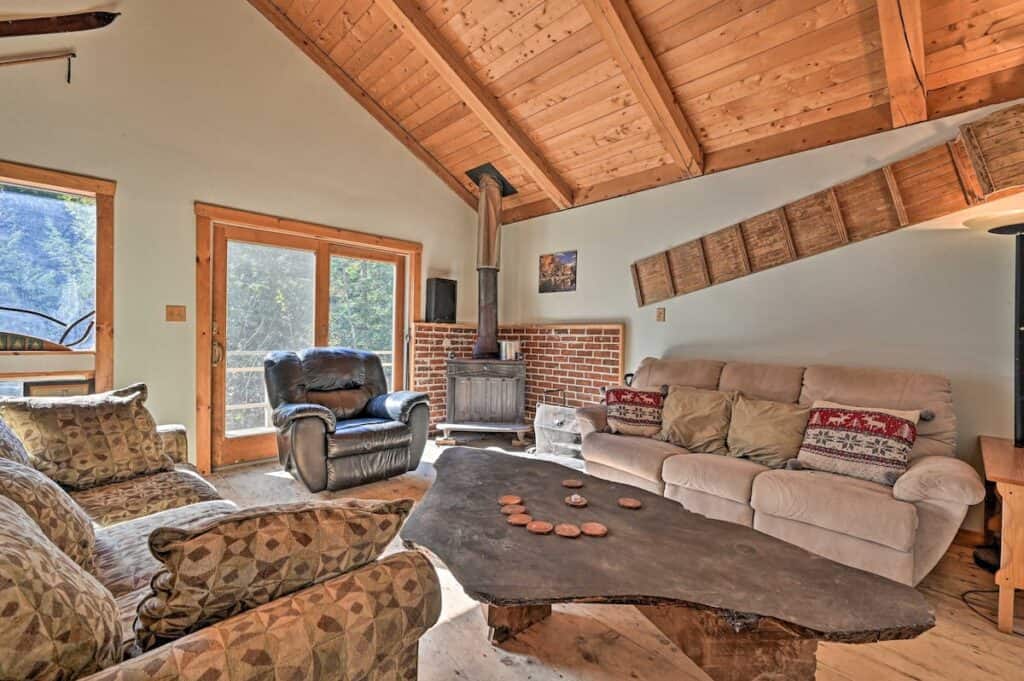 Living room with high, vaulted ceilings made of wood. A couch is set up next to a coffee table near a fireplace.
