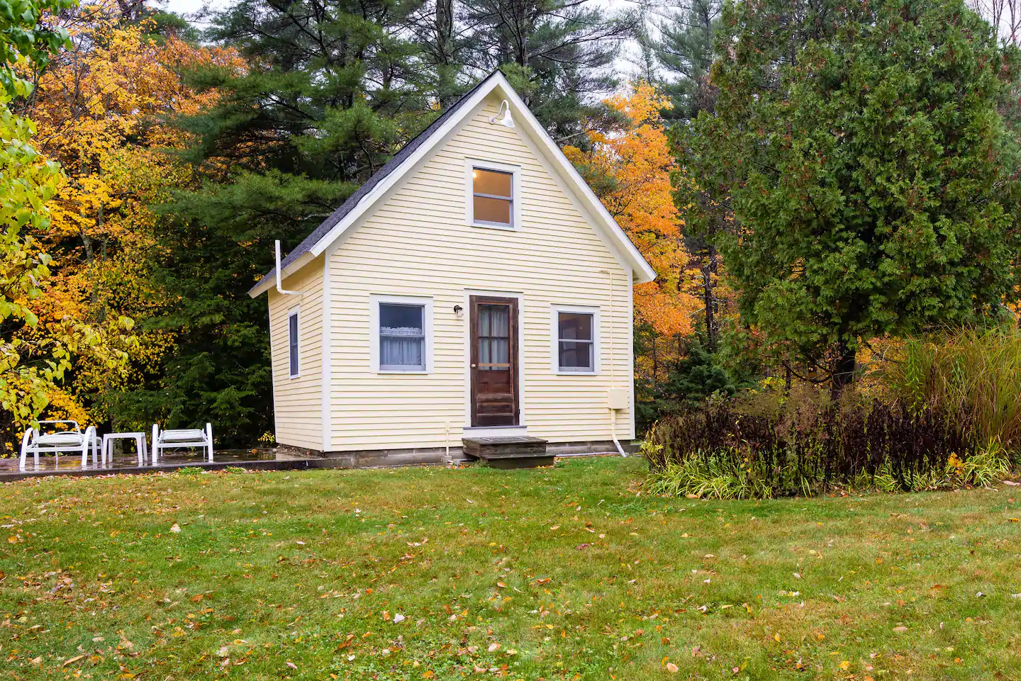 Yellow triangular house surrounded by a forest. The home has a wooden door in the middle and a window on either side. There\'s also a window up above the door, on the second floor.