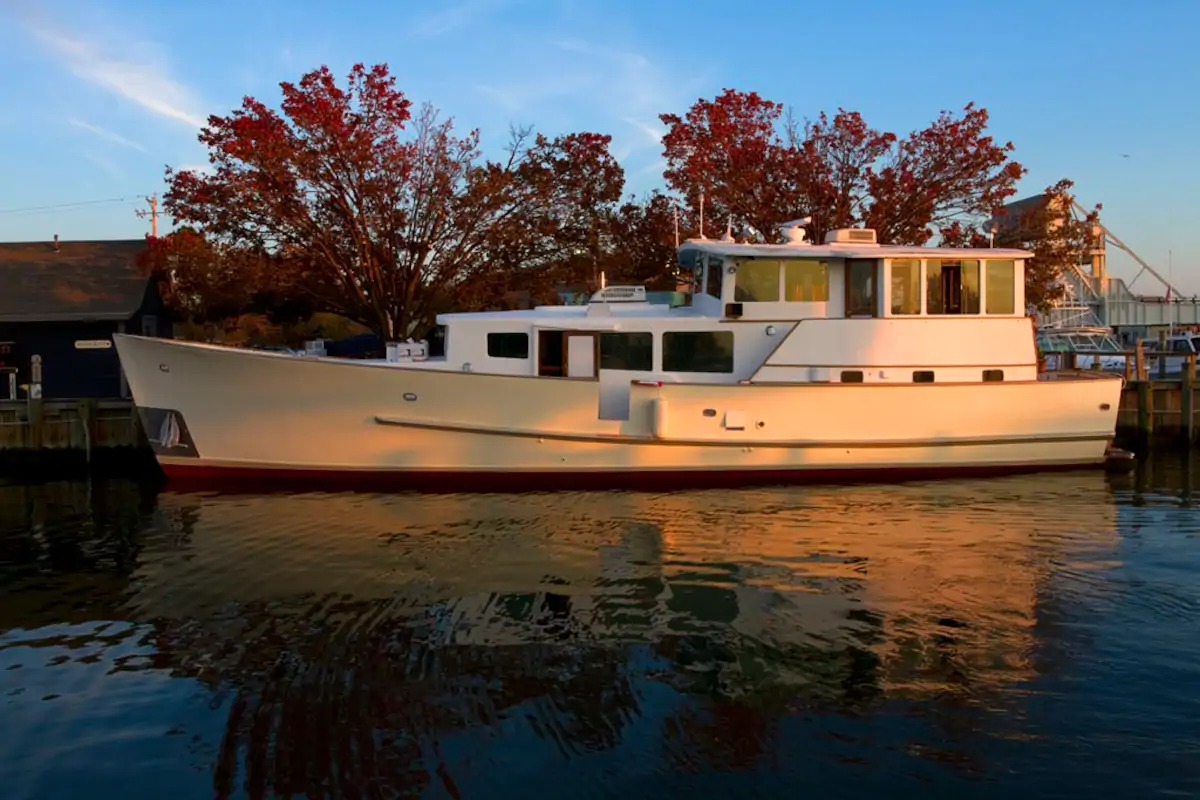 White boat floats on a lake with red trees surrounding the water under a blue sky.