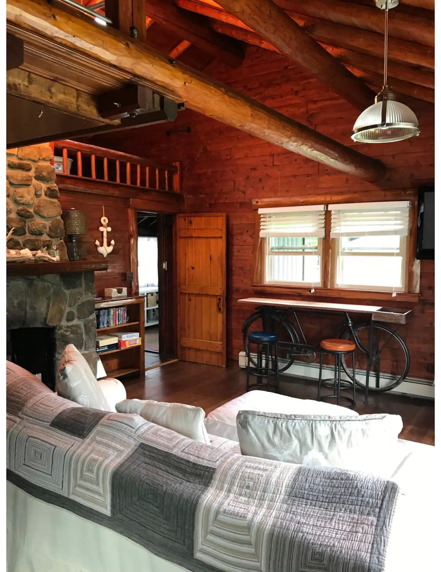 Couch facing a window in a wooden cottage. A grey quilted blanket is overlaid on the couch.