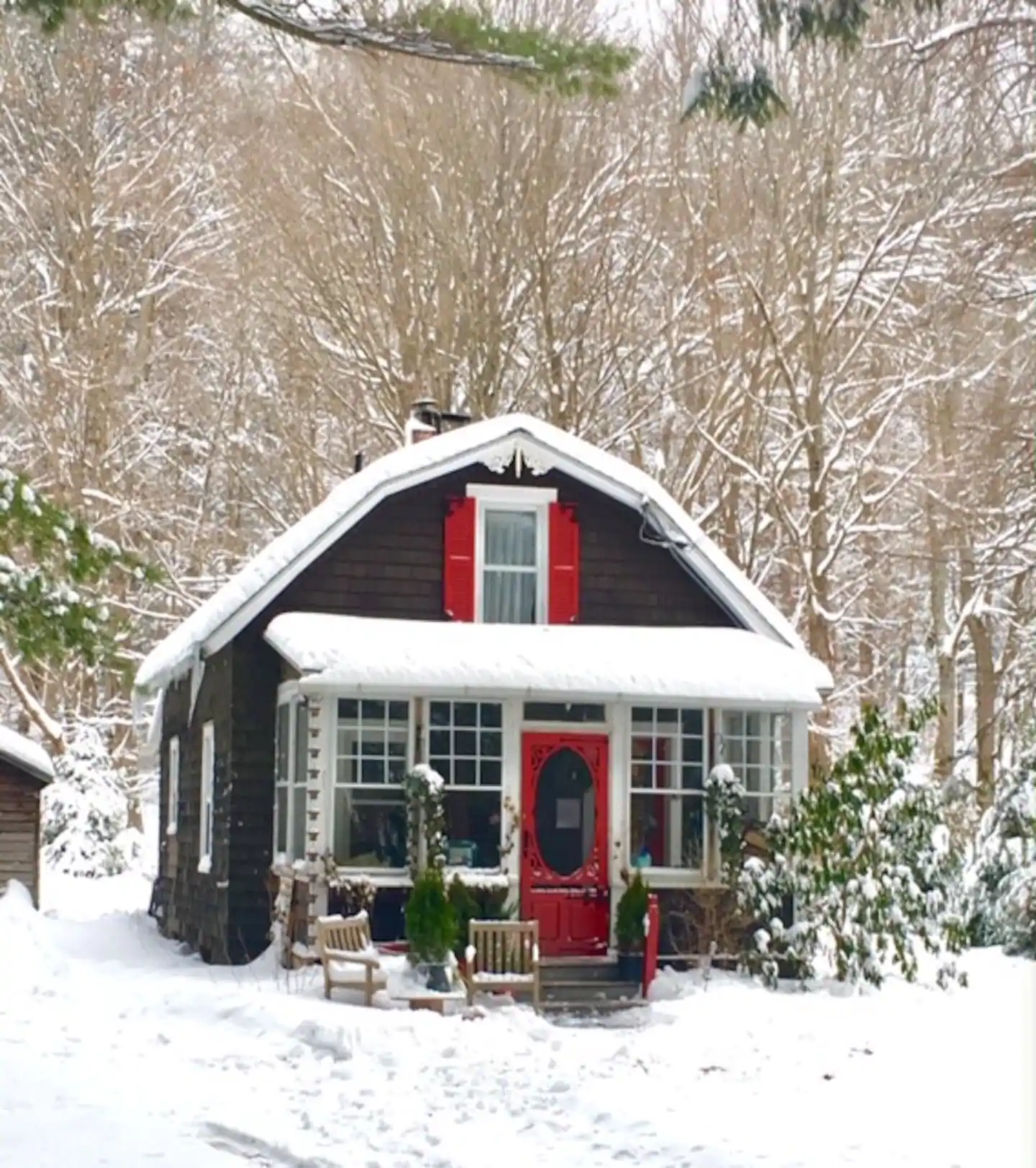 Brown house with a bright red door covered in snow. Behind the home are trees.