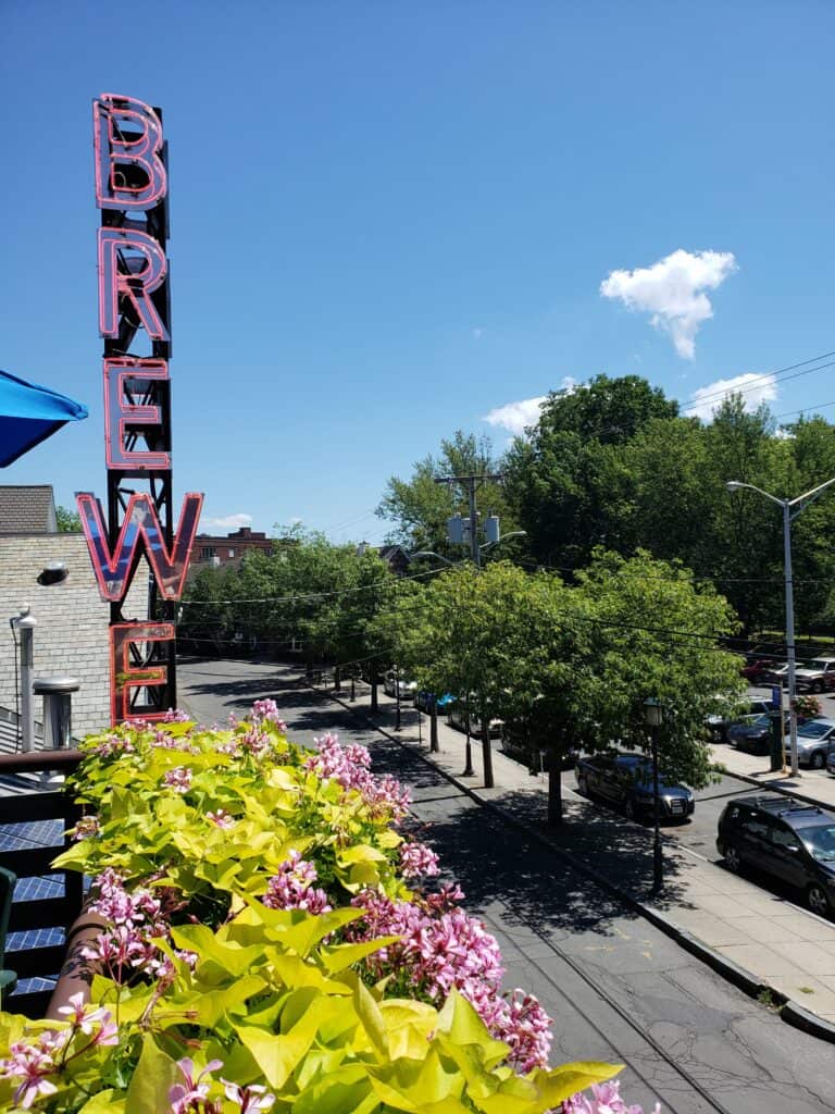 Pink neon sign during the day that says \"brewery\" attached to a building near the street.