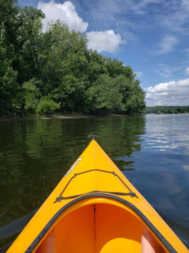 Orange kayak floating on a lake under a blue cloudy sky.