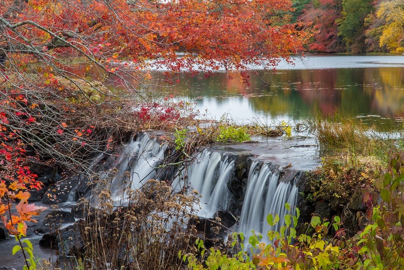 Lake leading to a waterfall surrounded by fall foliage.
