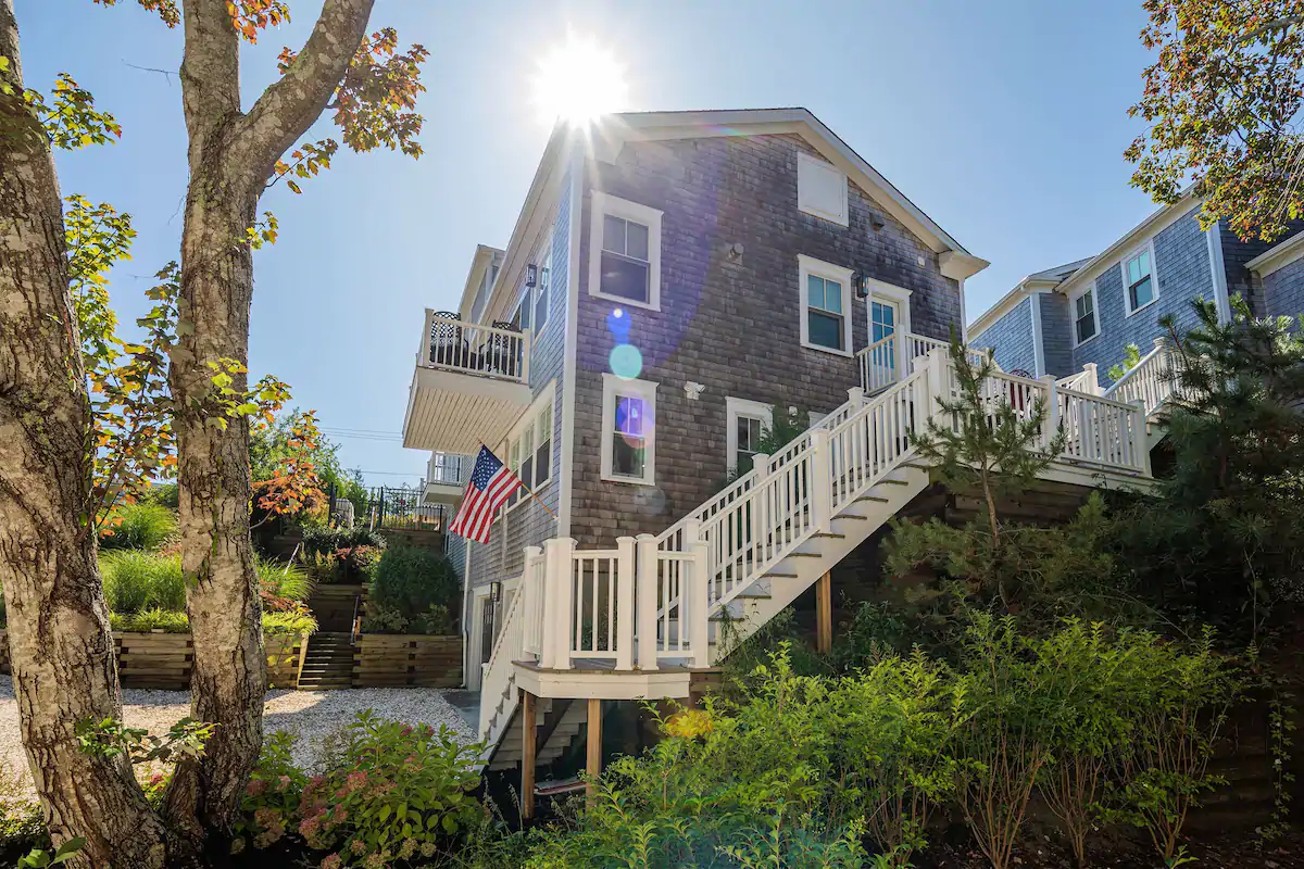 Large 3 story stone house with a long flight of white stairs with railings going up to the 3rd floor.