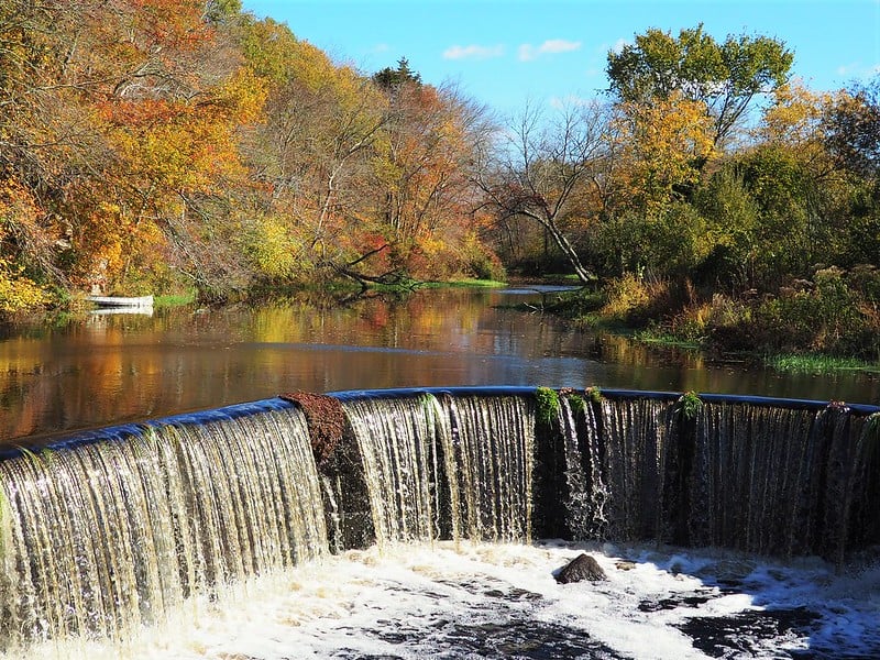 Lake leading to a small waterfall surrounded by fall foliage.