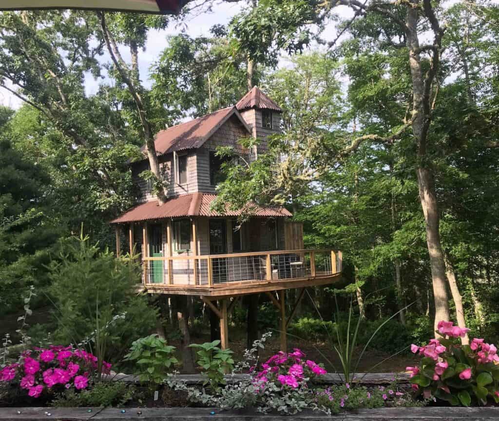 A two story treehouse surrounded by trees and flowers