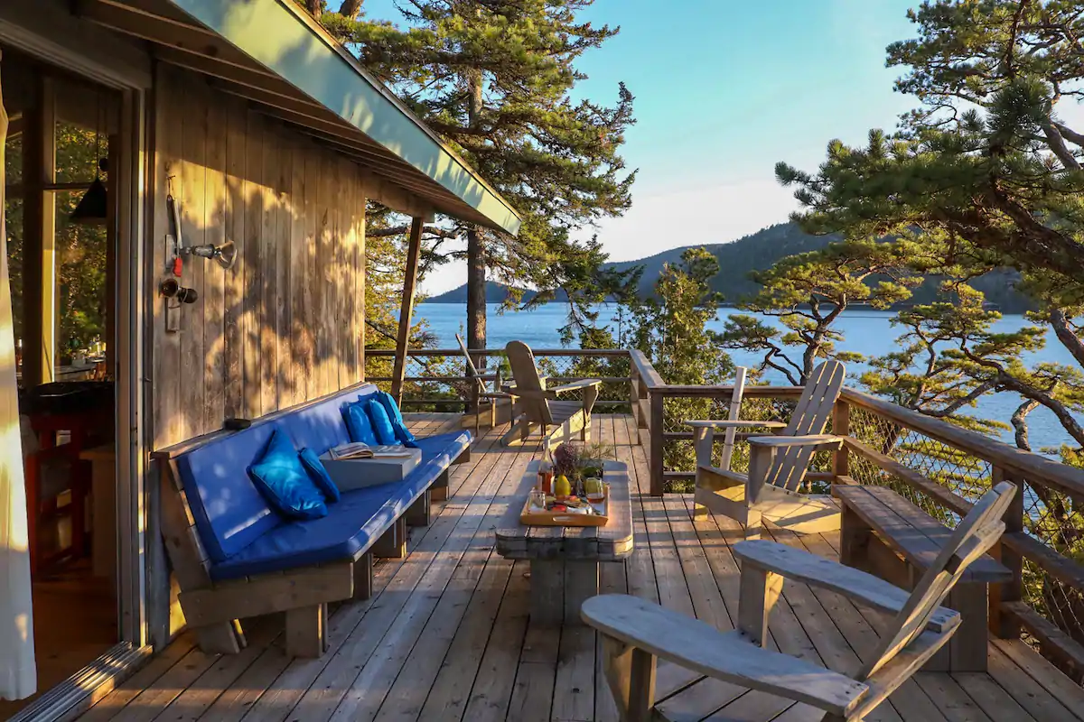 Outdoor furniture sits on a wooden porch with the water and mountains seen in the background.