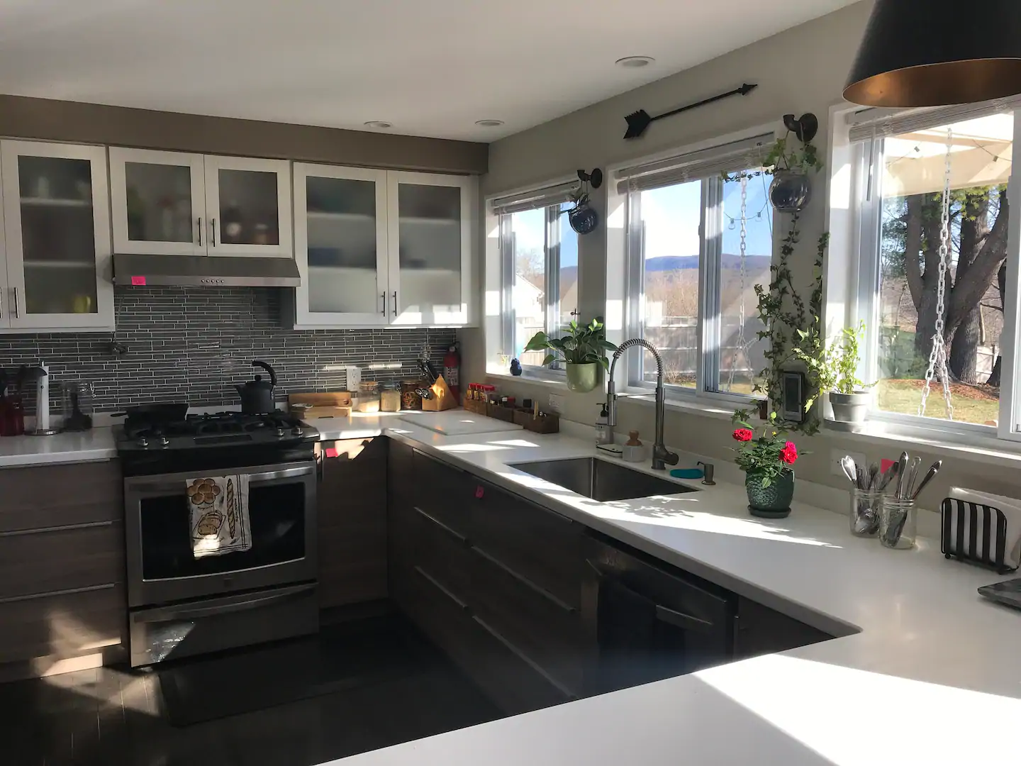 Interior view of a kitchen with white tops and cabinetry. Light is coming in through the windows next to the sink.