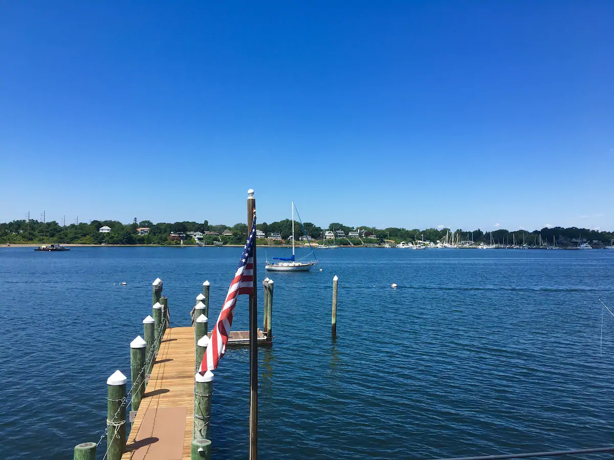 Empty dock leading to the ocean. Boats float on the water in the distance under a blue sky.