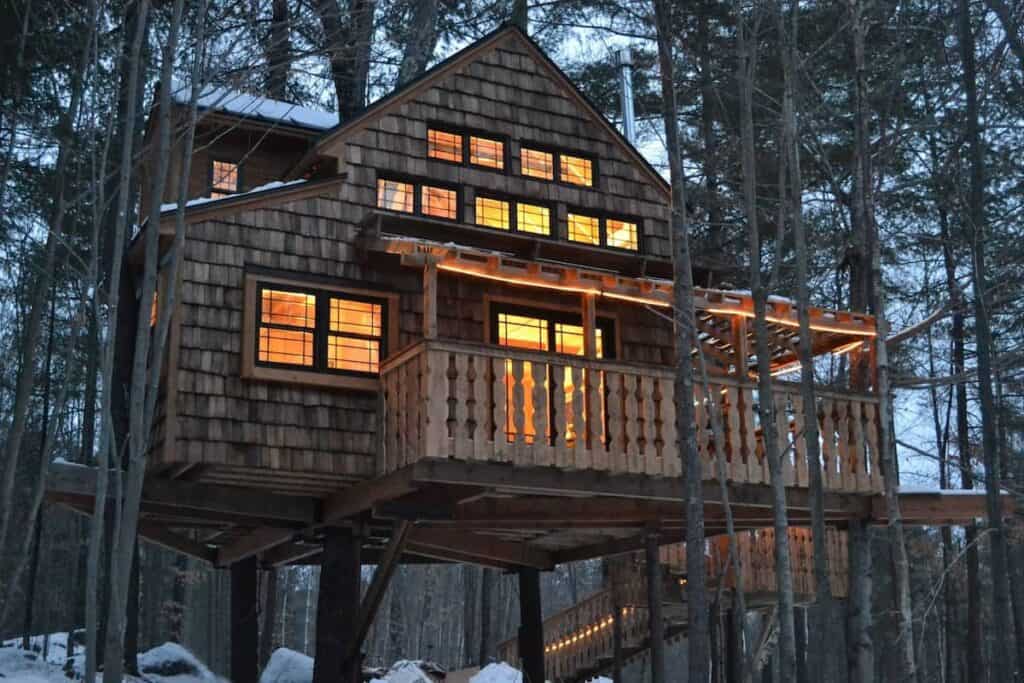 A treehouse with lights on inside and trees around it