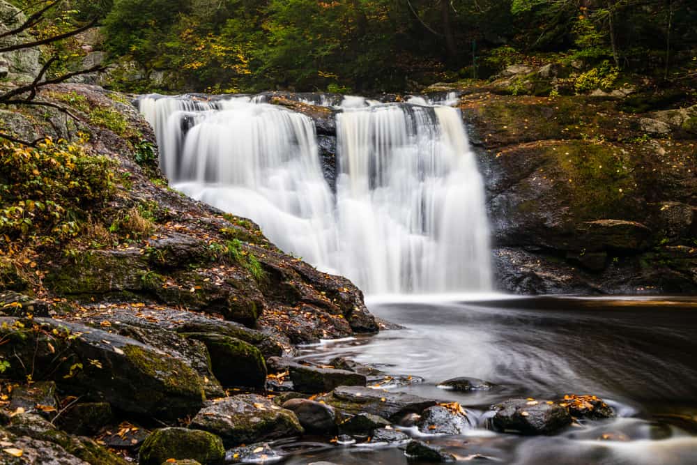 Large, wide waterfall cascading into a rocky pond by lush greenery.