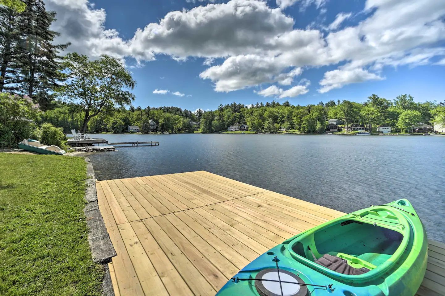Blue and green kayak sitting on a wooden dock by the lake. The lake is surrounded by a forest in the distance.
