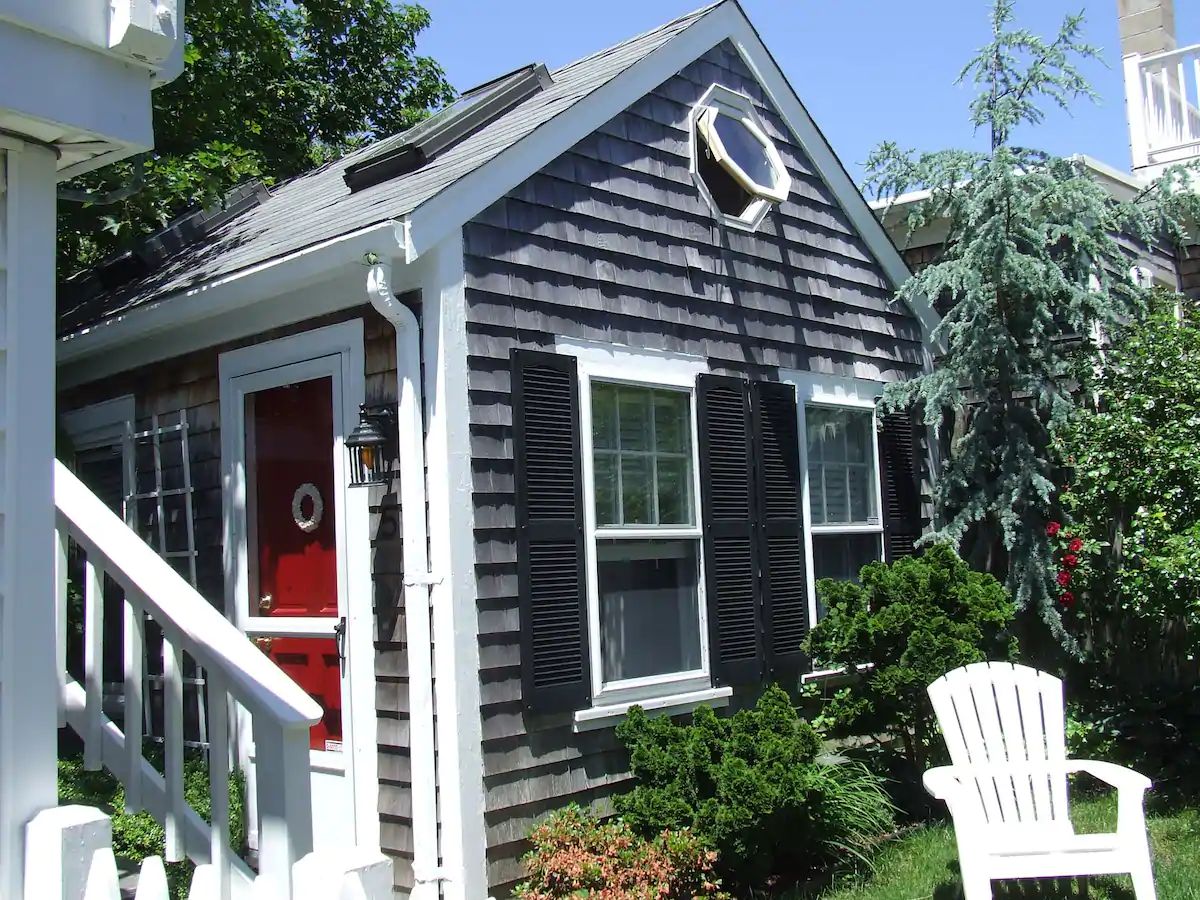 Grey cottage with black window shades under a blue sky.