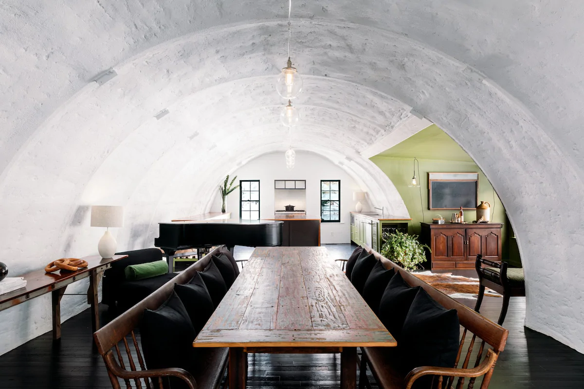 Wooden table surrounded by benches with black pillows in a domed room.