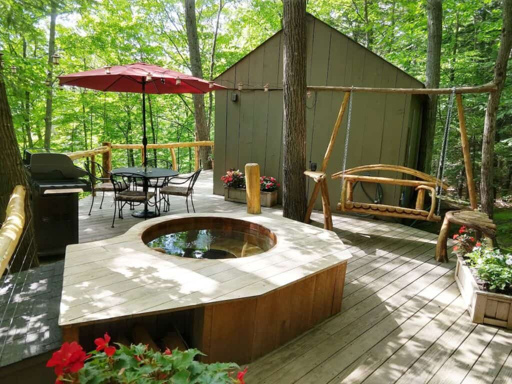 A hot tub on a wooden deck with a wooden swing and table and chairs with umbrella