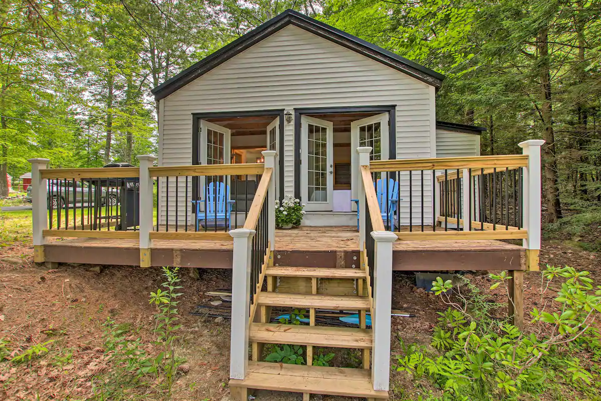 Cream home with black trim in the forest. Wooden stairs lead up to the home\'s deck, and the doors are open, welcoming people in.