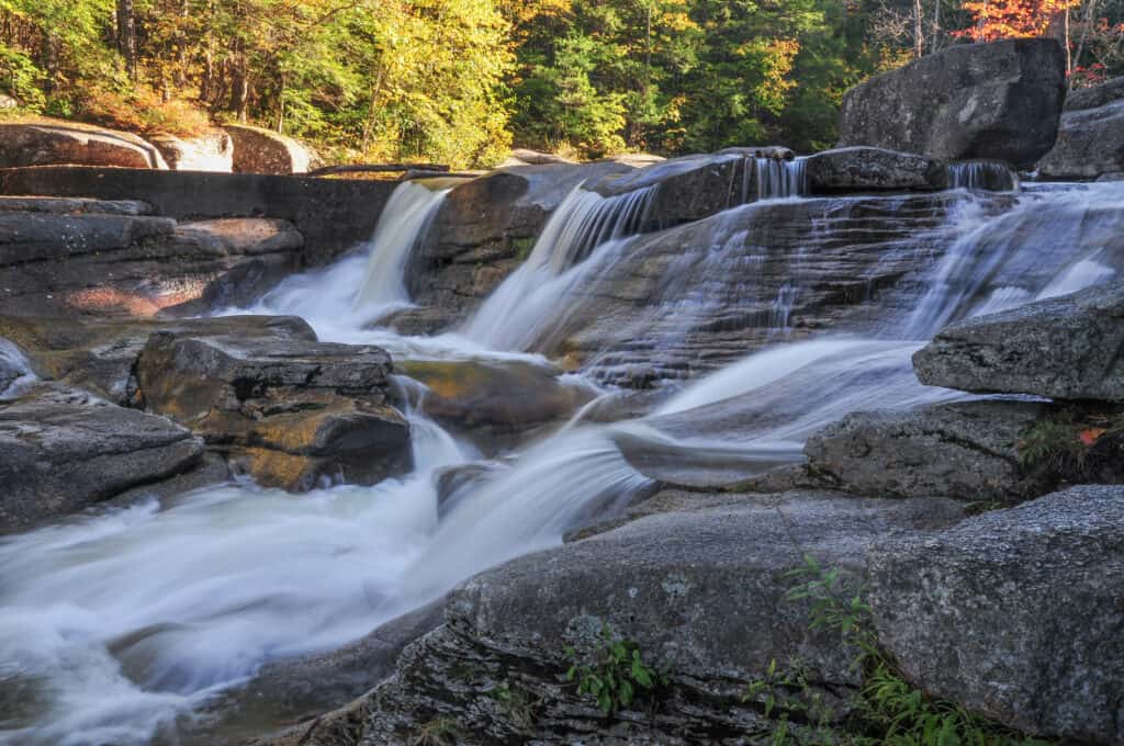 Multiple waterfalls stream down rocks into more water. Trees can be seen in the background.