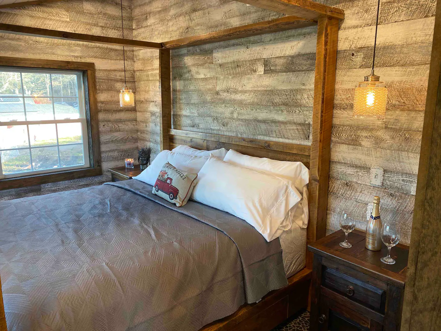 Wooden bed with grey bedding in a room with wooden walls. 