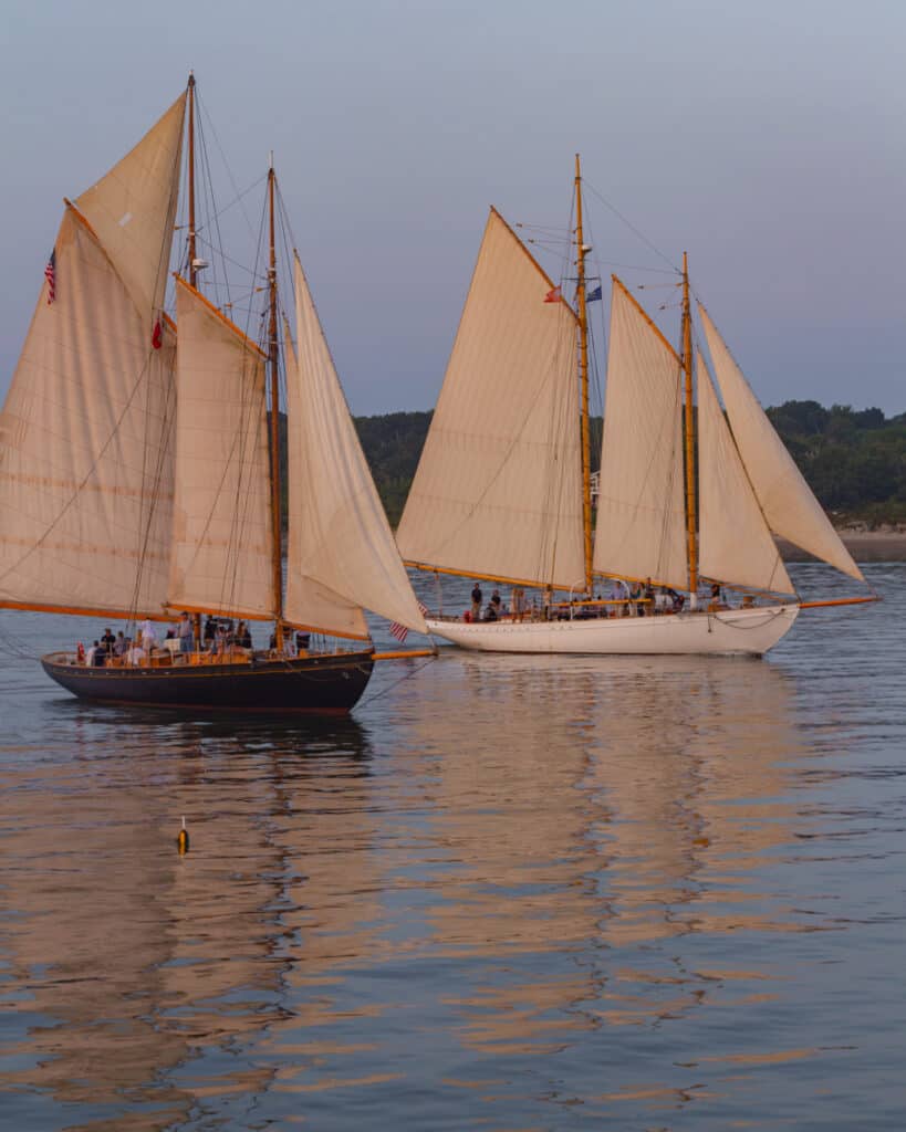 Two boats filled with people floating on the water under a grey sky.