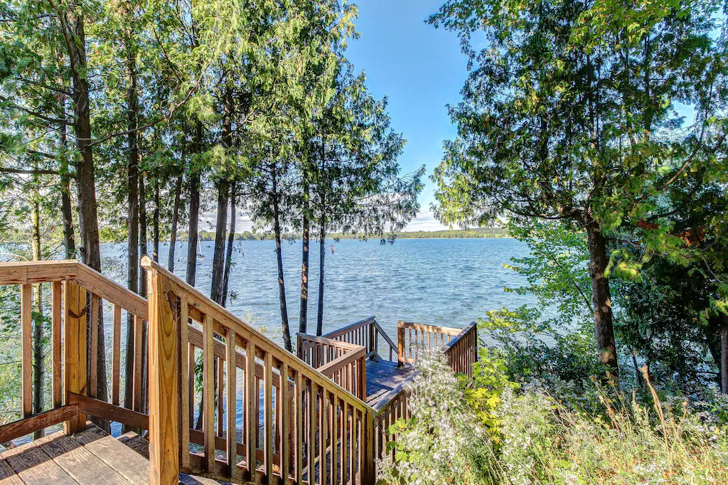 Wooden stairway leading down to a dock with chairs looking at a body of water on a sunny day