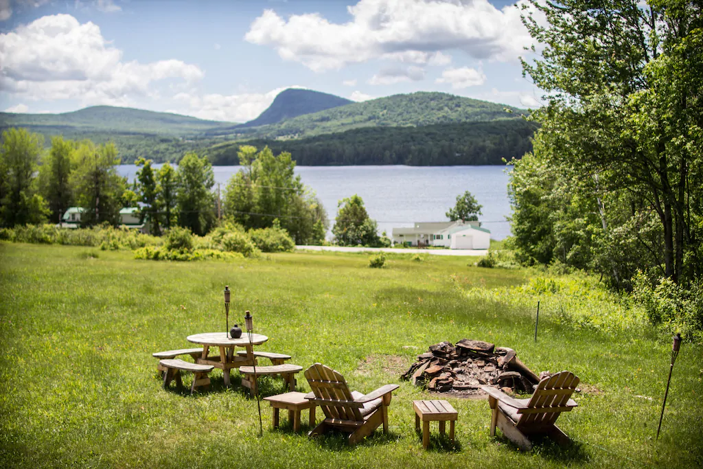 Adirondack chairs and picnic table on a lawn overlooking a body of water with mountains in the distance at one of the prettiest New England VRBOs