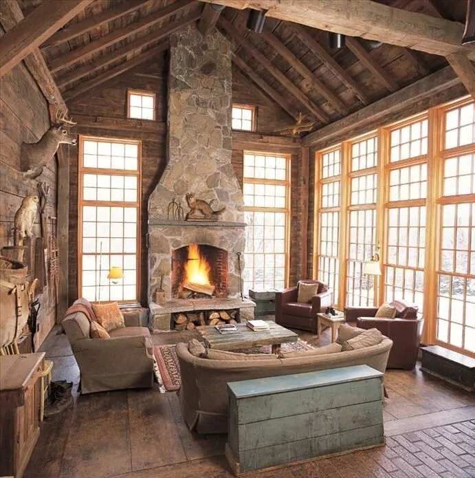 A living room with walls of windows and a stone fireplace in the center