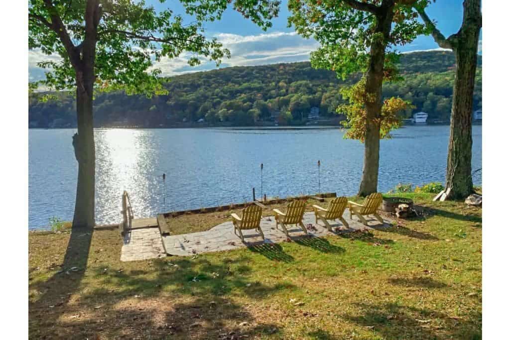 Wooden chairs and steps leading into a body of water on a sunny day with a mountain in the distance at one of the most popular lake VRBOs in New England