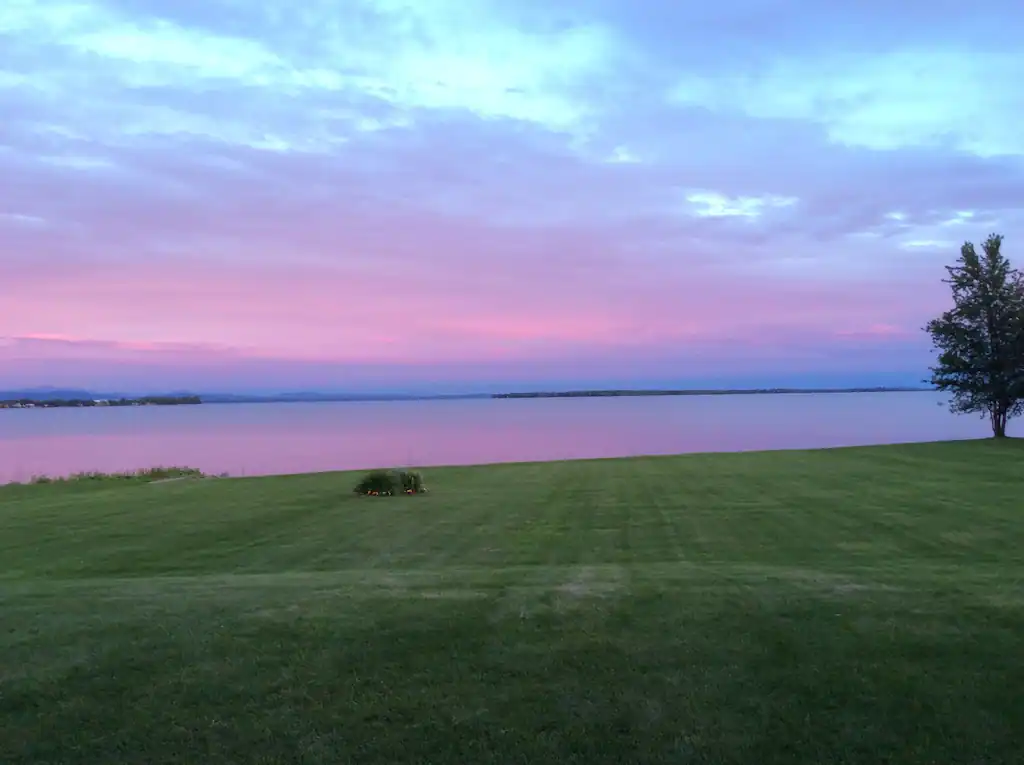 A grassy expanse extends out towards a lake at sunset with skies of lavender, dusty rose, and blue