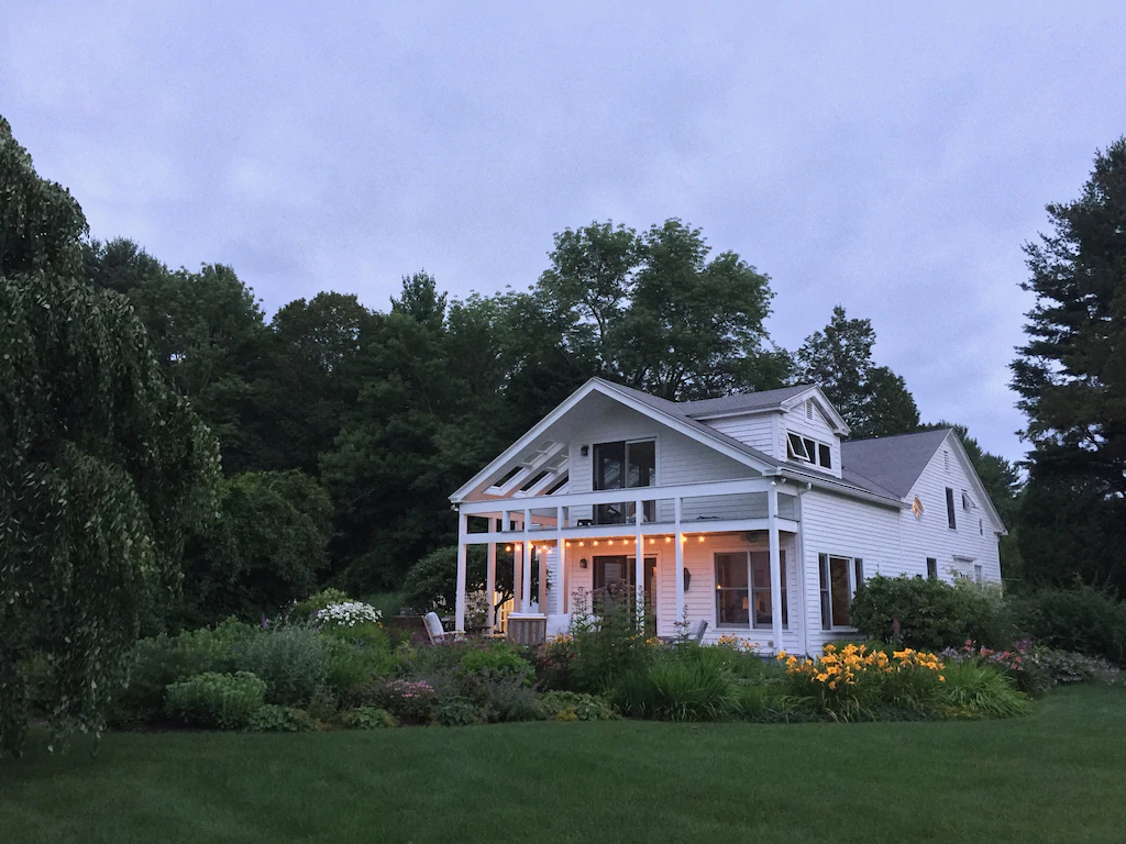 Large white vacation rental surrounded by shrubbery, lawn and trees is one of the best VRBOs in New England