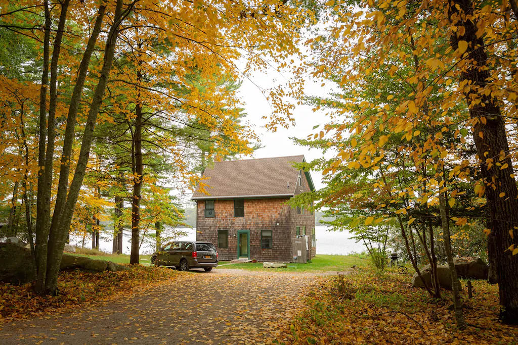 Saltbox style New England vacation rental on a dirt road surrounded by Autumn trees