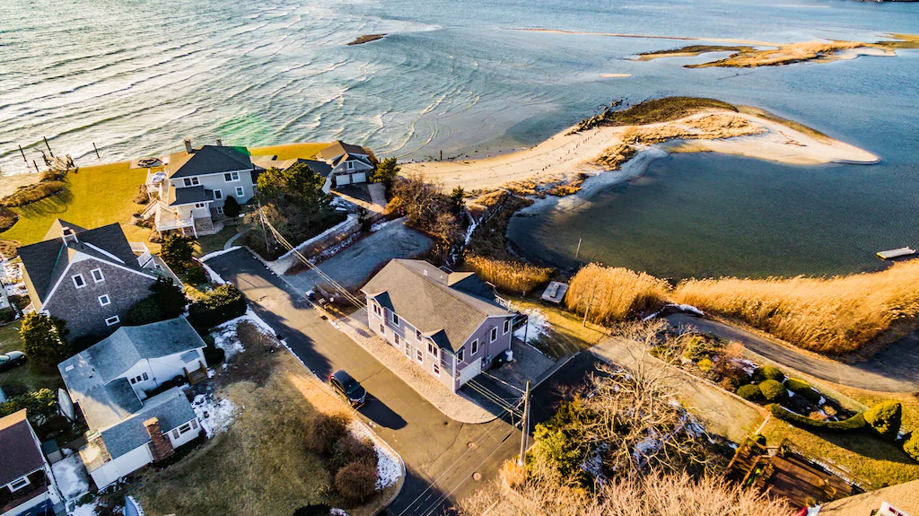 Aerial view of mansion at the edge of a beach and a body of water at a beachfront VRBO in New England