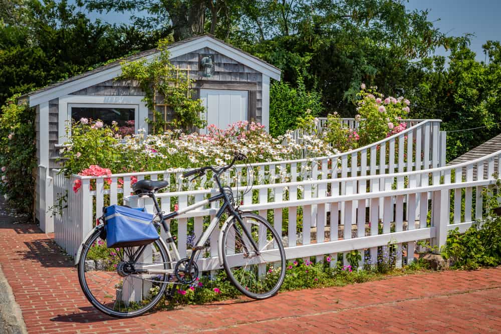 A bicycle parked in front of a white picket fence and a grey and white house