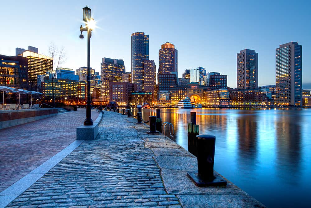 Lit streetlamp next to the water in Boston Harbor with the city lit up in the distance