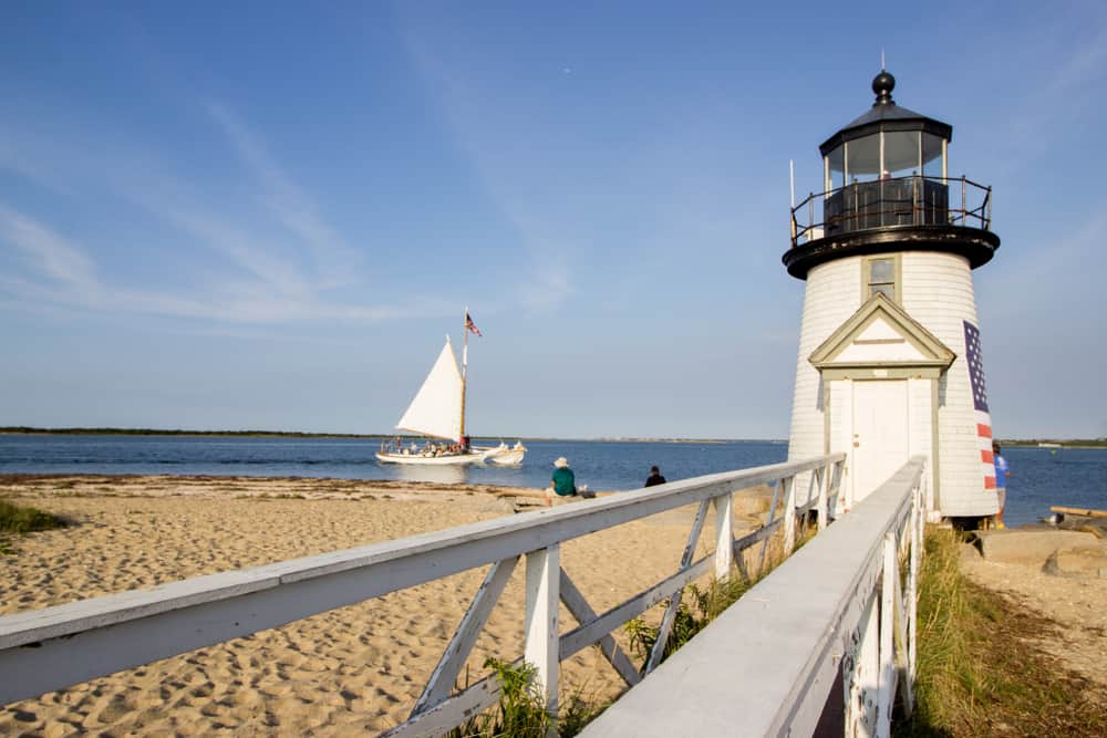 A lighthouse on the beach in Nantucket with a sailboat in the water