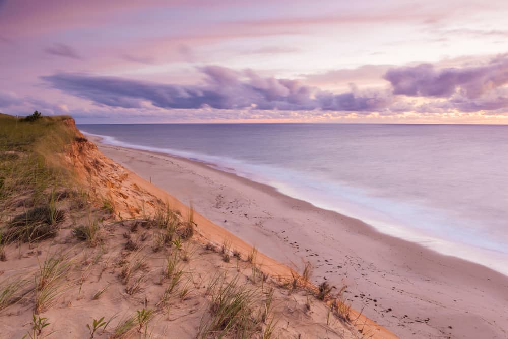 Sandy beach at the water\'s edge with a pink and purple sky