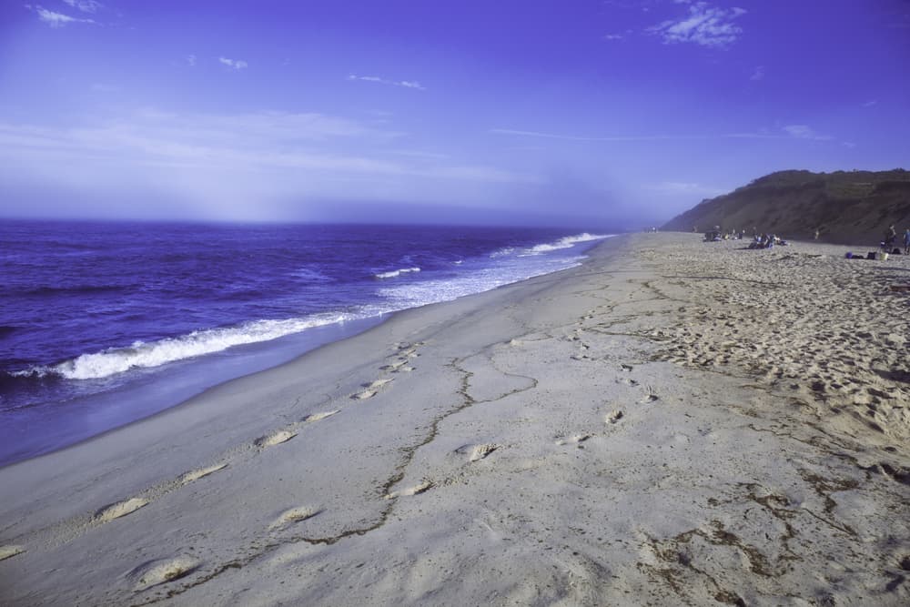 Large sandy beach with the blue ocean on the left and waves rolling in 