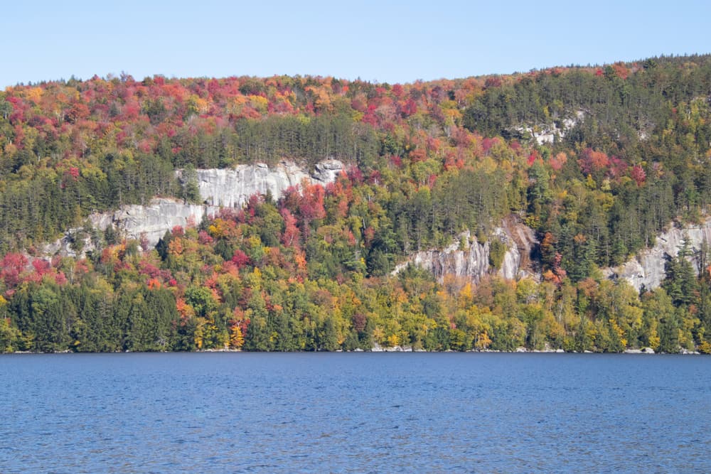 A large body of water with a mountain of fall trees in the background