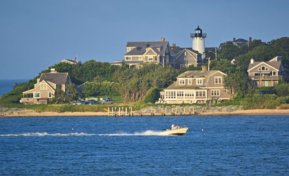 A small boat in a large body of water with a lighthouse and houses on the shore