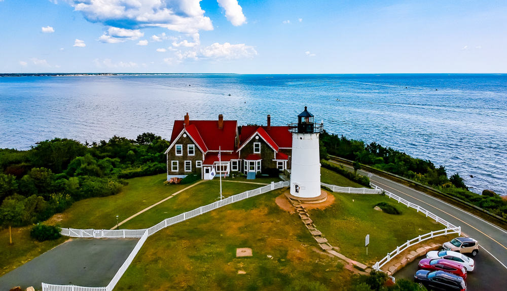Aerial view of white lighthouse next to a red house overlooking the ocean