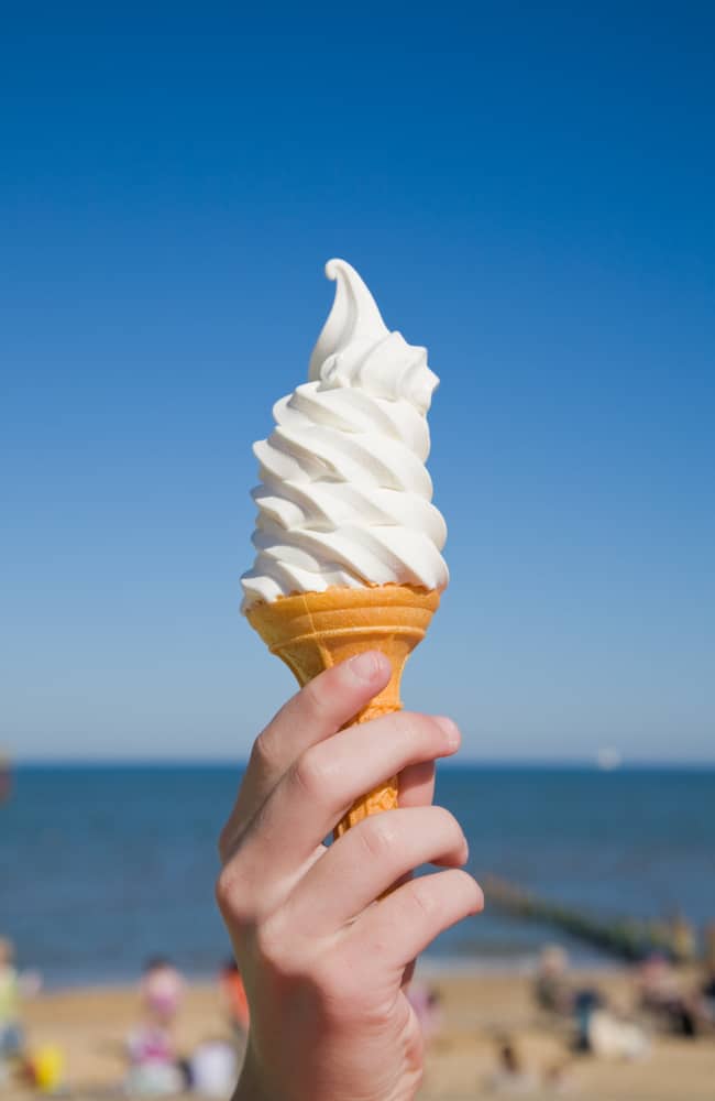 Closeup of white soft serve ice cream cone with a background of blue water and sky