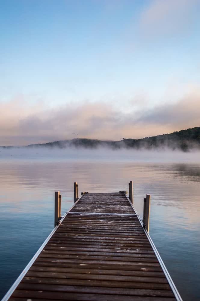 A wooden pier leading to a body of water that is reflecting pink from the sunset