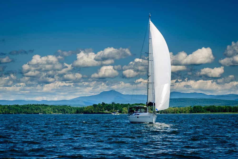 A sailboat in a large body of bright blue water on a clear day with fluffy white clouds in the sky