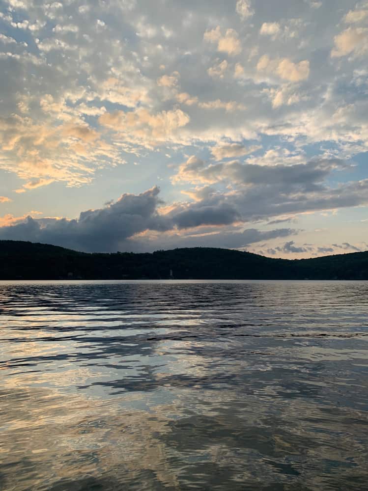 A large body of water at sunset with a silhouette of mountains in the distance 