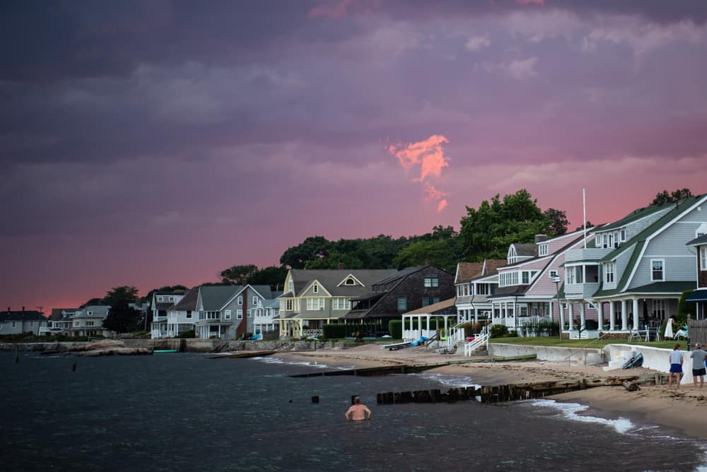 A row of houses on the shore with people swimming in the water