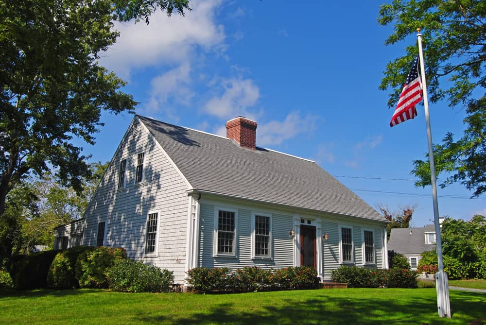 A white cape cod style house with a green lawn out front