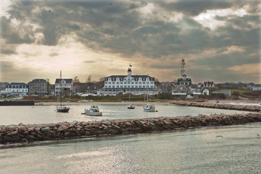 A body of water divided by a strip of land covered with rocks with boats and a town in the distance