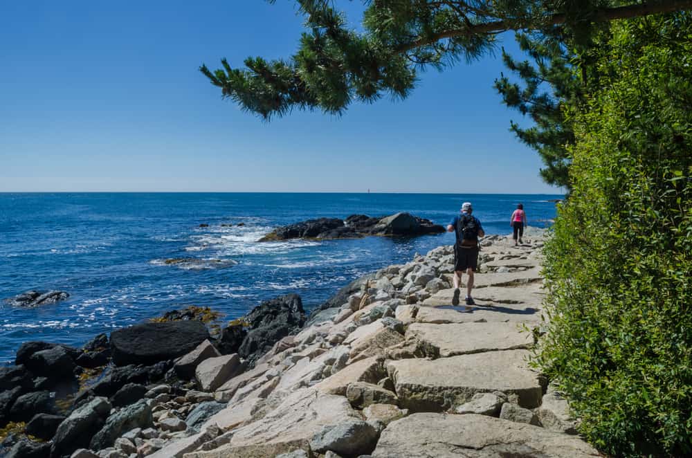 People walking on a rocky ledge next to the ocean in Rhode Island