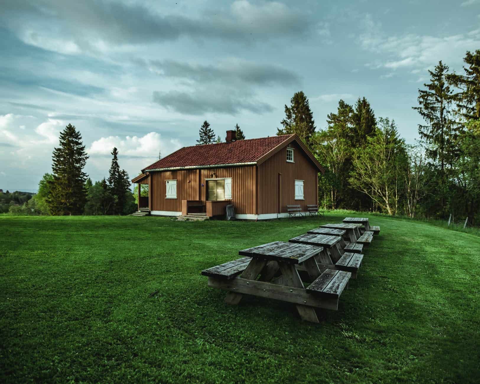 A row of wooden picnic tables on a big green lawn in front of a brown house